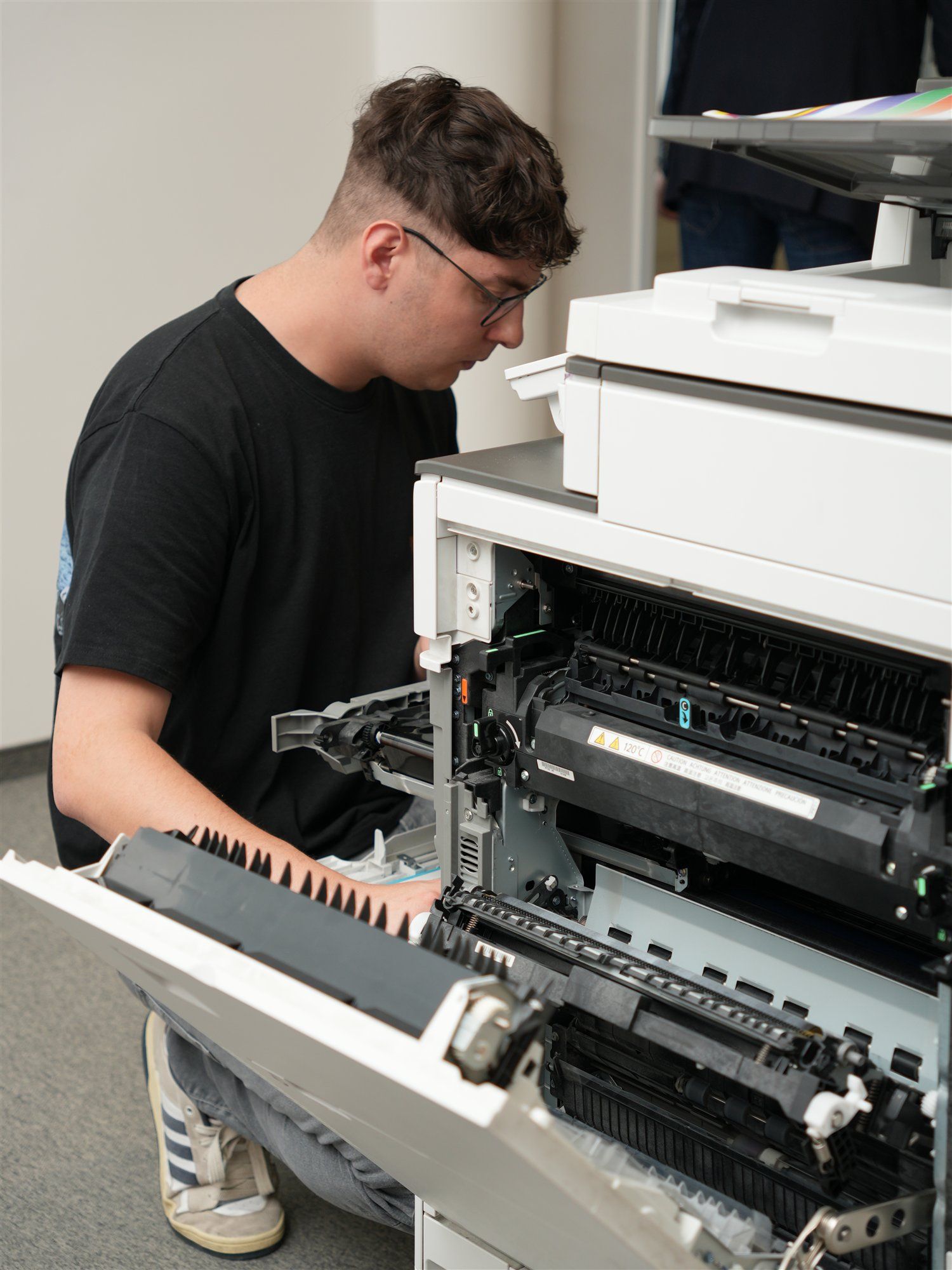 Holzer-Techniker kniet vor einem geöffneten Multifunktionsgerät und prüft das Innere