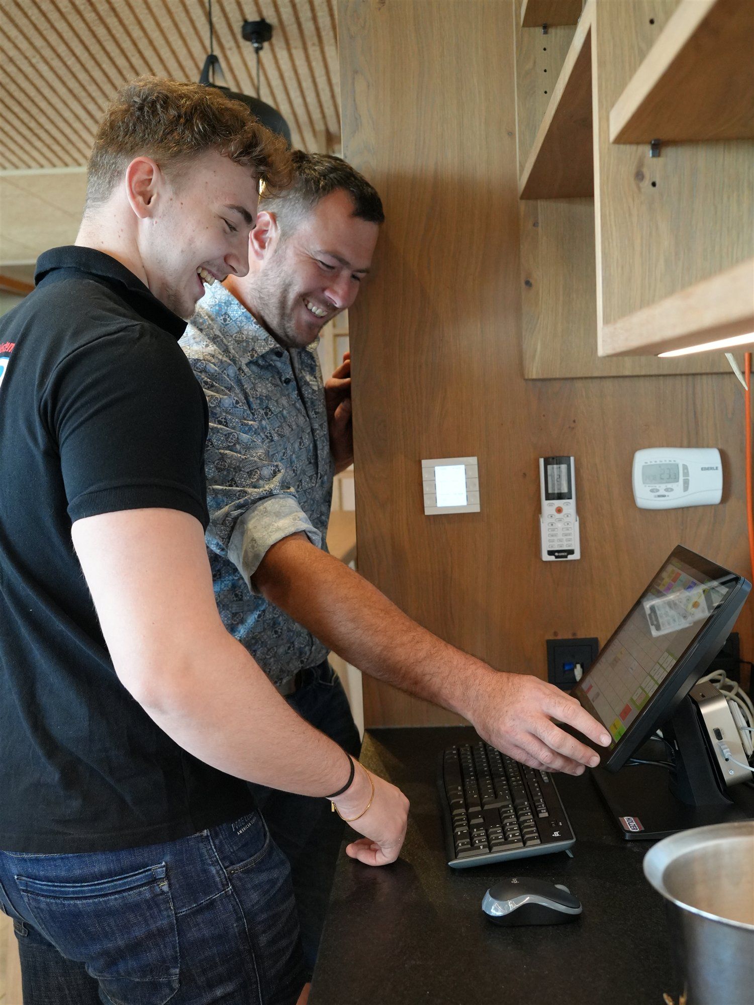 Holzer-Techniker und ein Kunde lachen gemeinsam an der Touchscreen-Kassa in einem Weingut