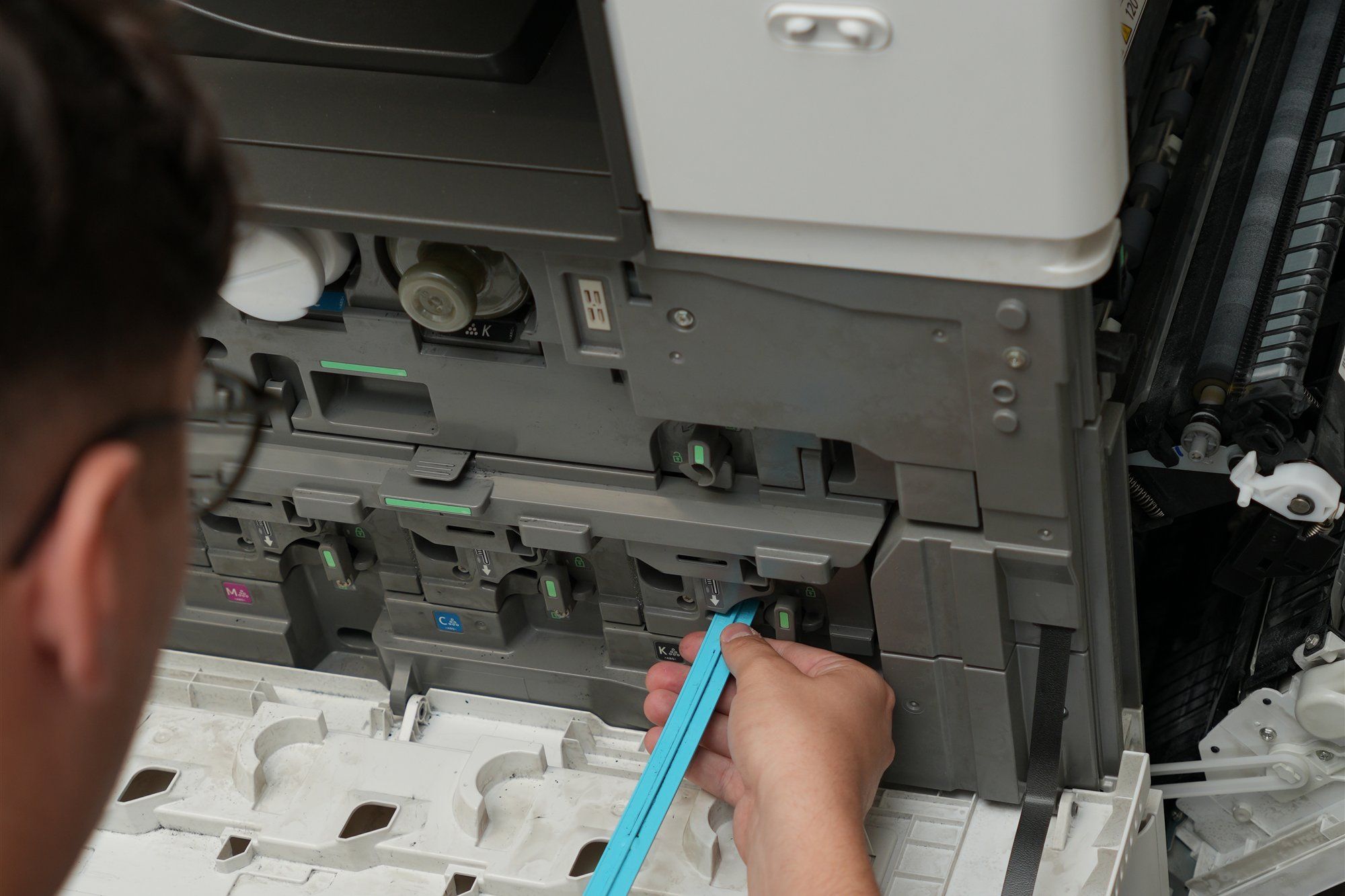 Holzer-Techniker arbeitet mit einem blauen Werkzeug im geöffneten Tonerbereich eines Multifunktionsgeräts