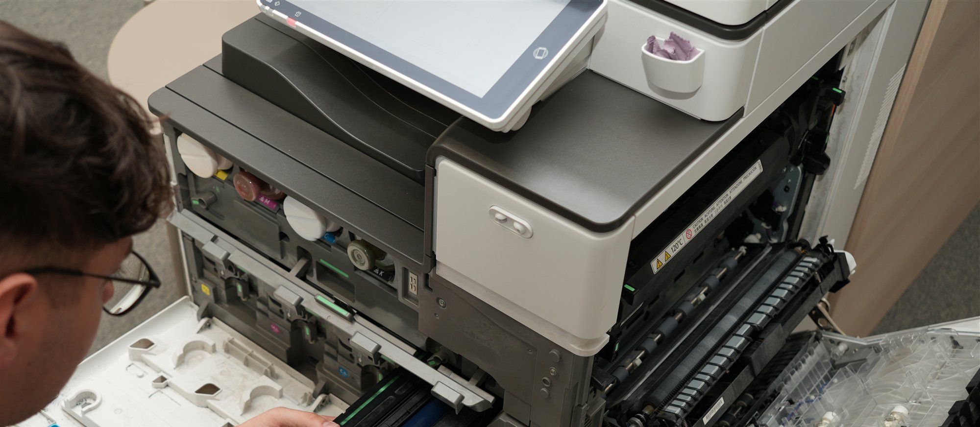 Geöffnetes Ricoh-Multifunktionsgerät mit Touch-Bedienfeld und offenen Klappen, links ein Holzer-Techniker