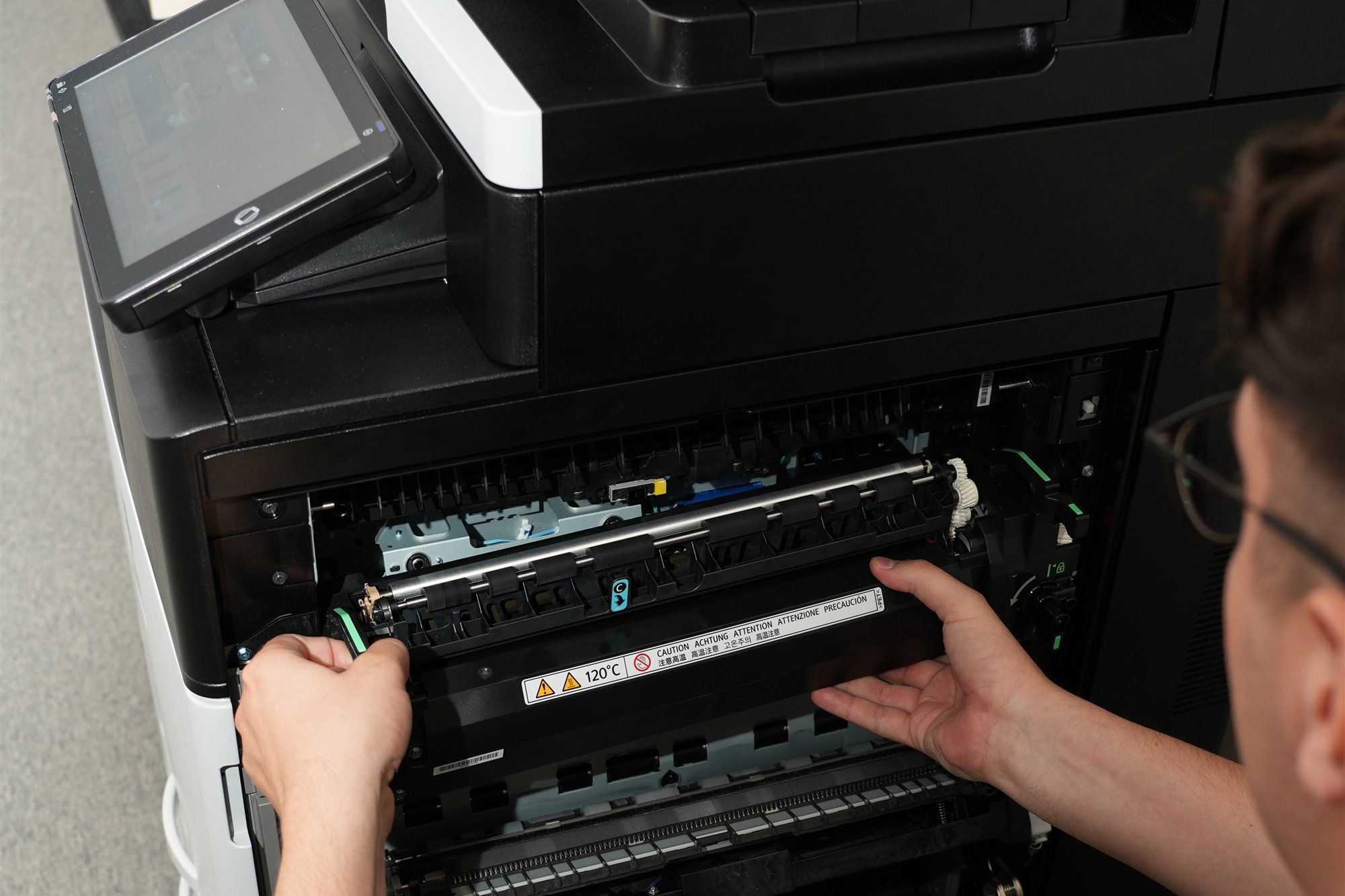 Holzer-Techniker an der Fixiereinheit eines geöffneten Ricoh-Multifunktionsgeräts, oben links das Touch-Bedienfeld