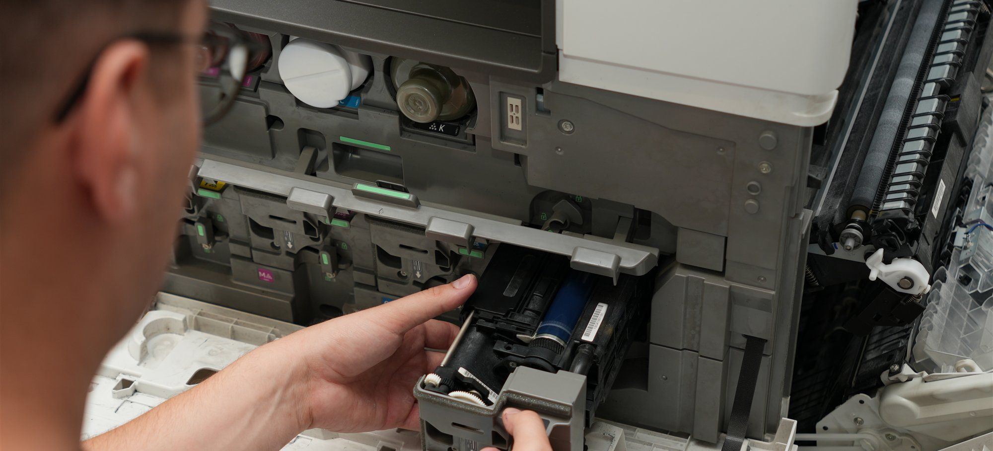 Holzer-Techniker tauscht bei der Wartung ein Bauteil in einem geöffneten Farbkopierer