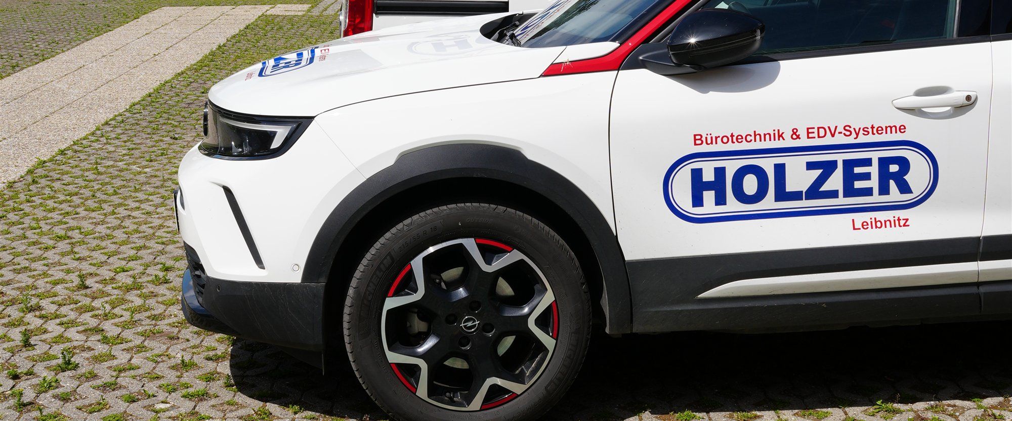 Weißer Holzer-Firmenwagen in der Seitenansicht, auf der Tür das Holzer-Logo mit der Aufschrift Bürotechnik & EDV-Systeme