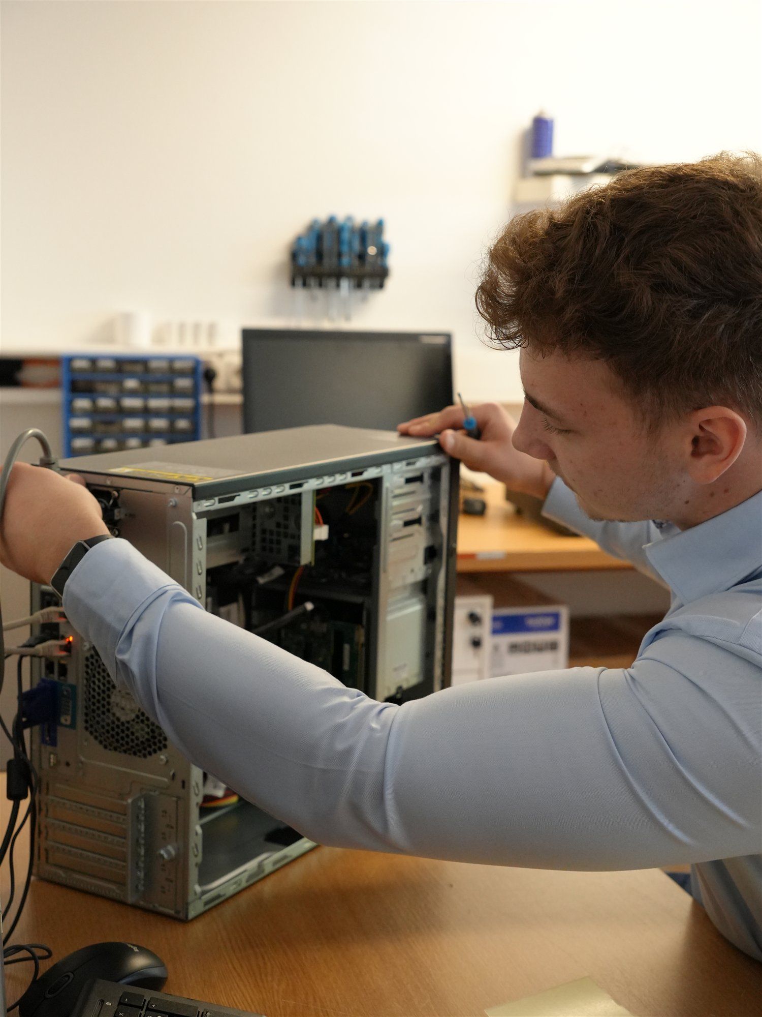 Holzer-Techniker arbeitet an einem geöffneten Computer, im Hintergrund eine Werkstattwand mit Schraubendrehern und Sortimentskasten