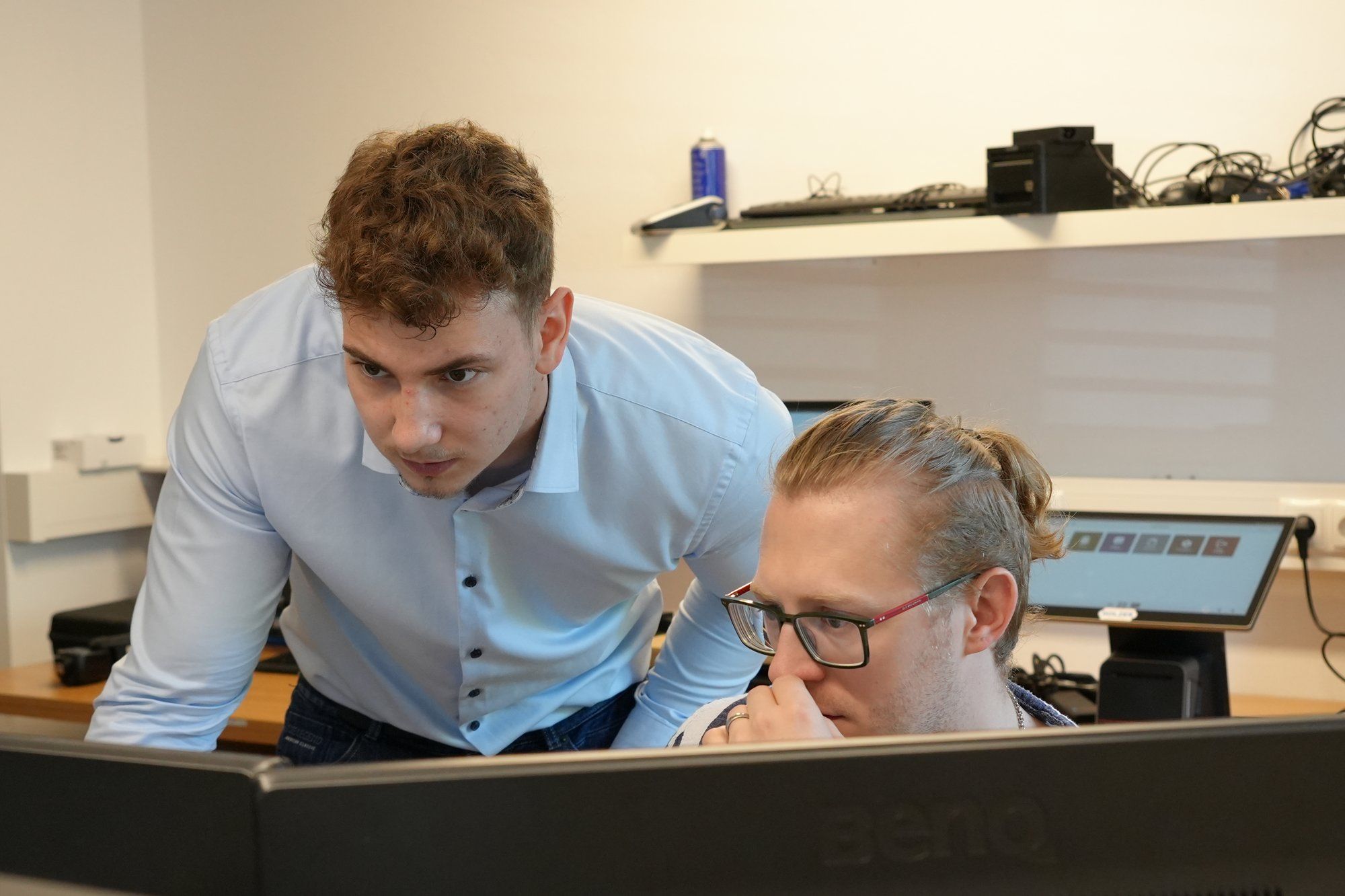 Holzer-Techniker beugt sich über die Schulter eines Kollegen, beide blicken konzentriert auf den Bildschirm