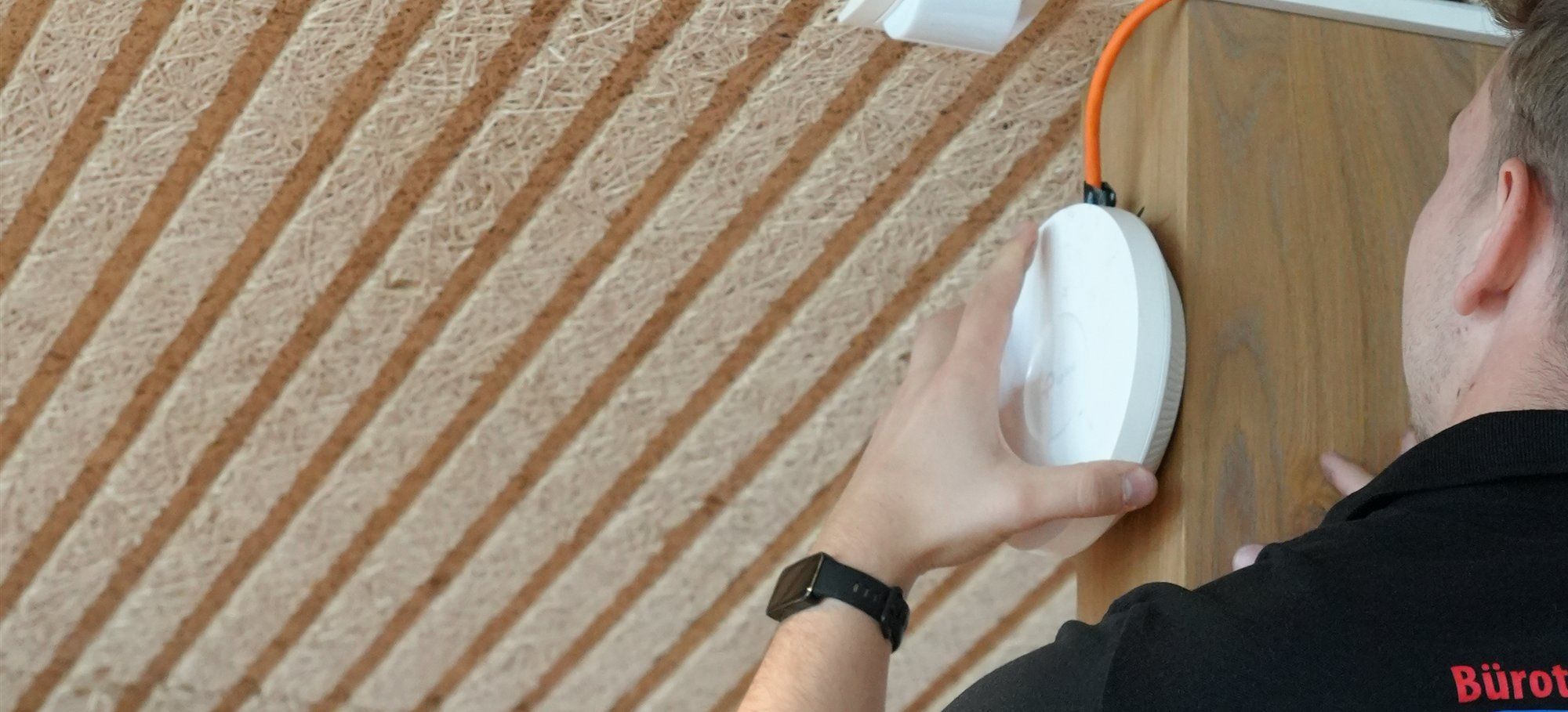 Holzer-Techniker befestigt einen WLAN-Access-Point mit Netzwerkkabel an einer Holzsäule unter der Decke