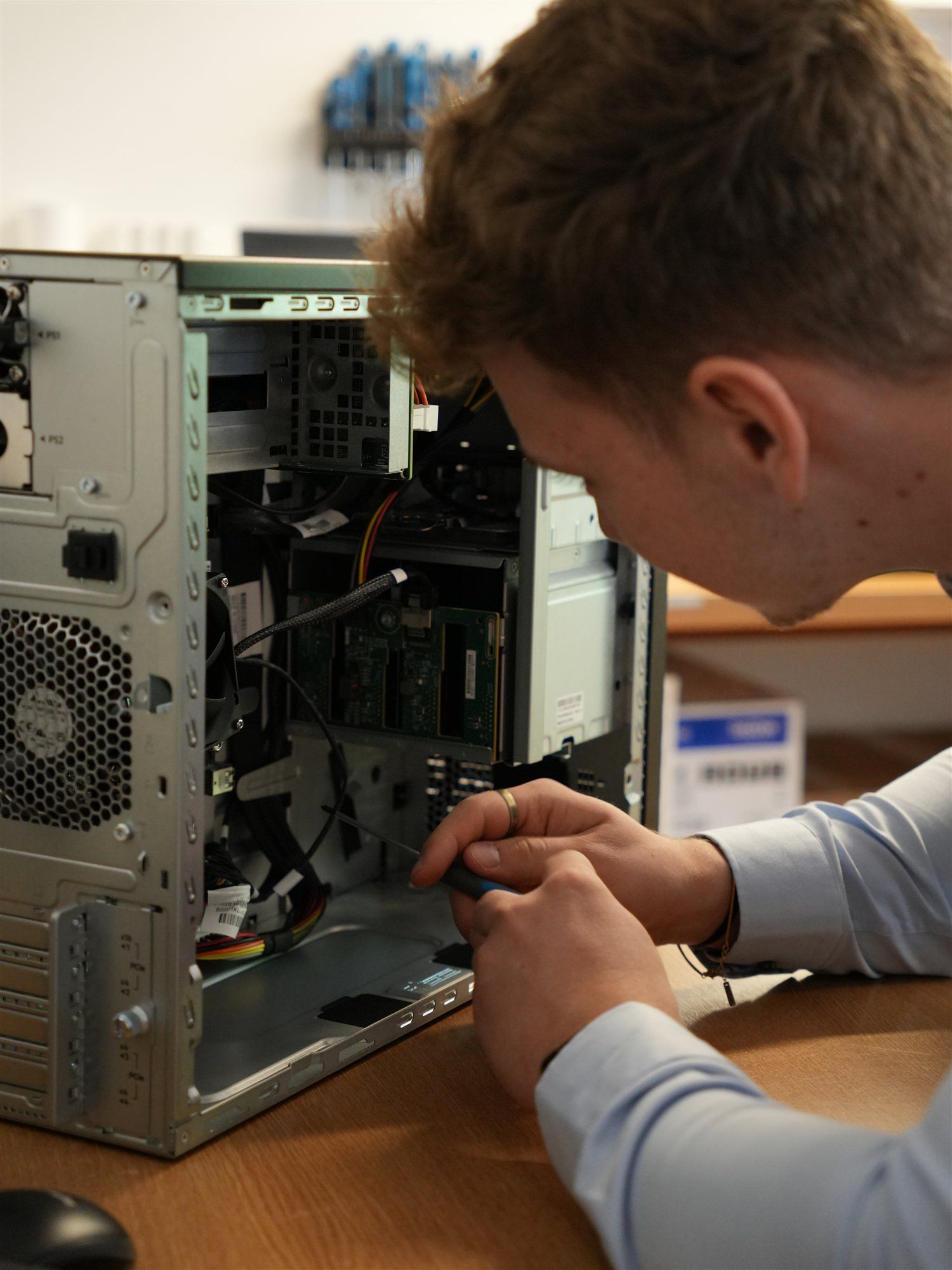 Holzer-Techniker beugt sich über einen geöffneten Tower-Server und setzt den Schraubendreher an