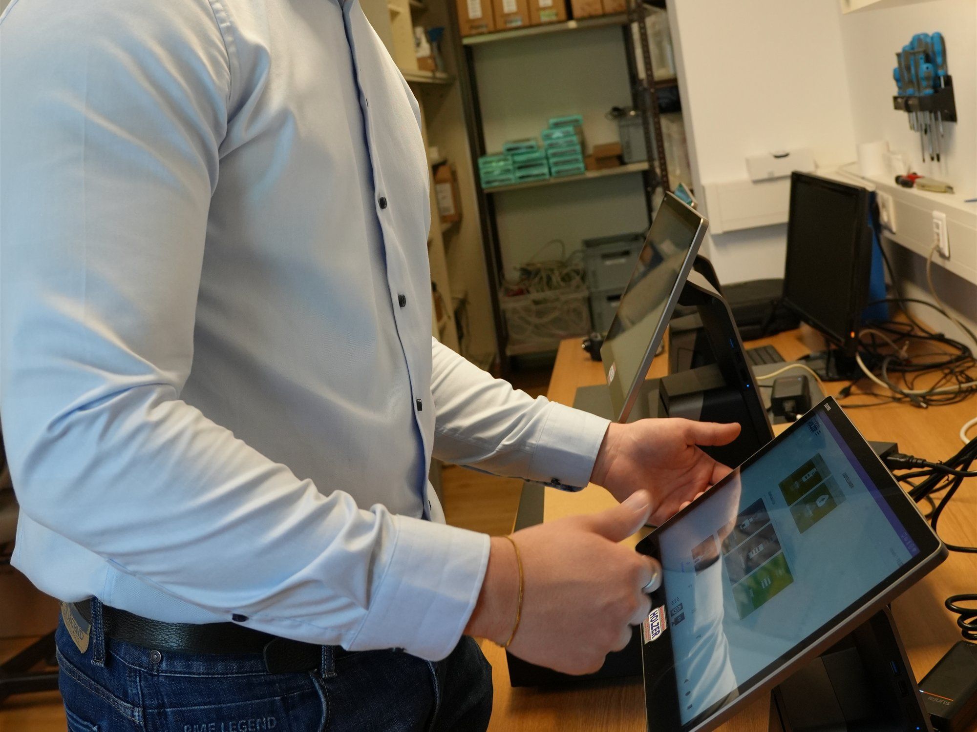 Holzer-Techniker hält ein Touch-Tablet auf dem Werkstatttisch und tippt auf den Bildschirm, im Hintergrund Regale