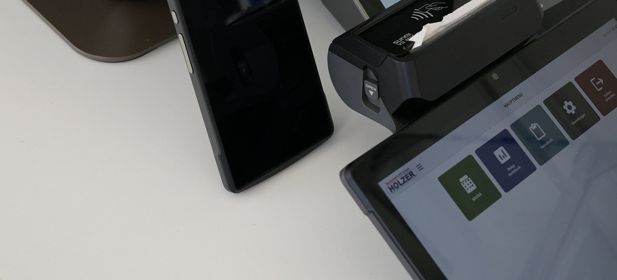 Kassenplatz mit Handgerät, mobiler Kassa mit Bondrucker und Tablet mit dem Hauptmenü der Holzer-Kassensoftware