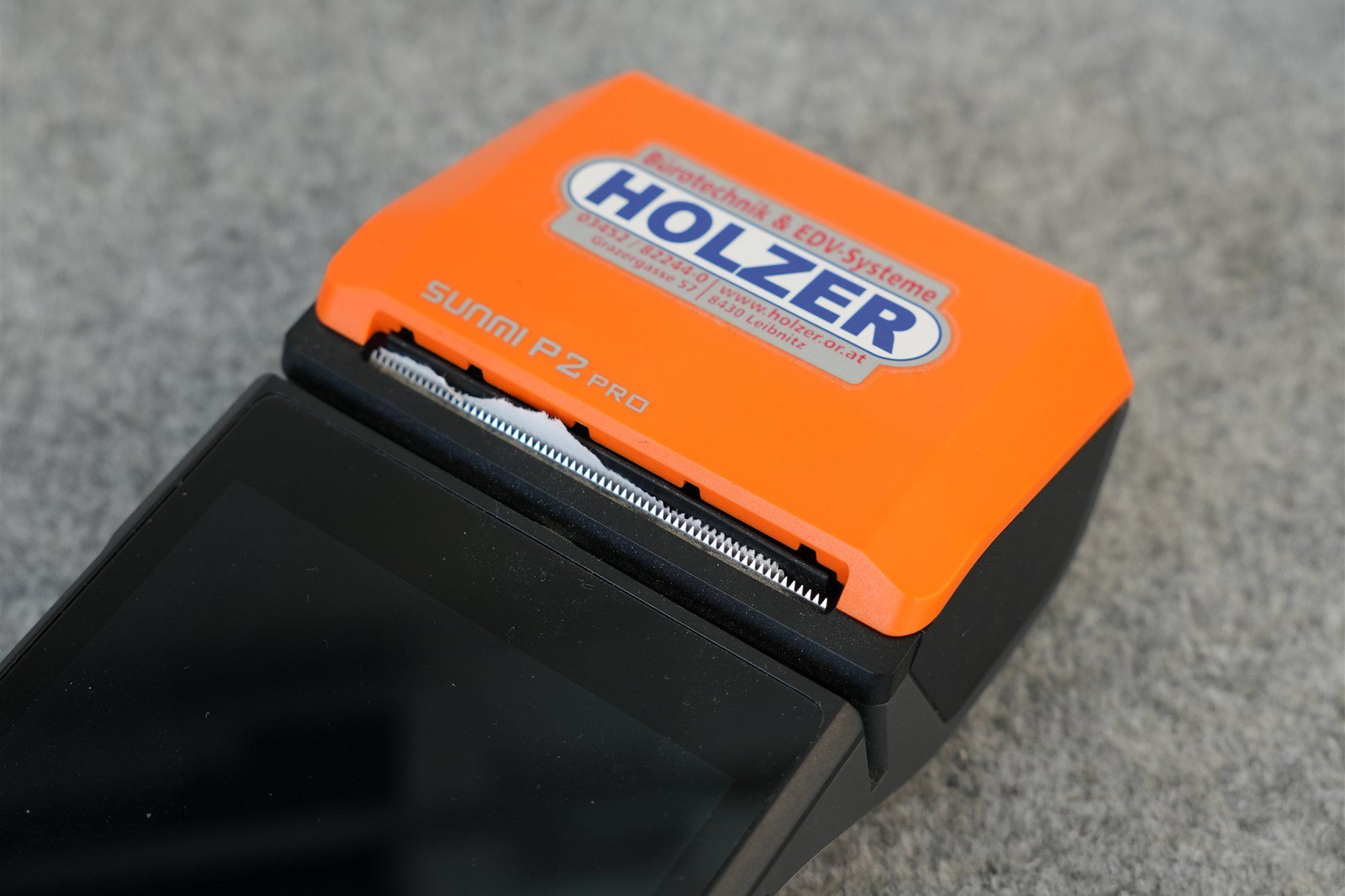 Mobile Kassa von Sunmi mit eingebautem Bondrucker und oranger Abdeckung mit Holzer-Aufkleber