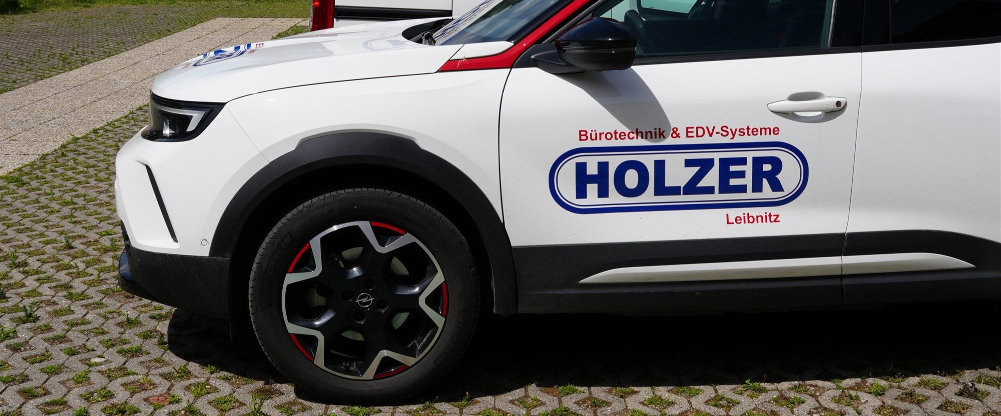 Seitenansicht eines weißen Holzer-Firmenwagens mit Firmenlogo auf der Tür