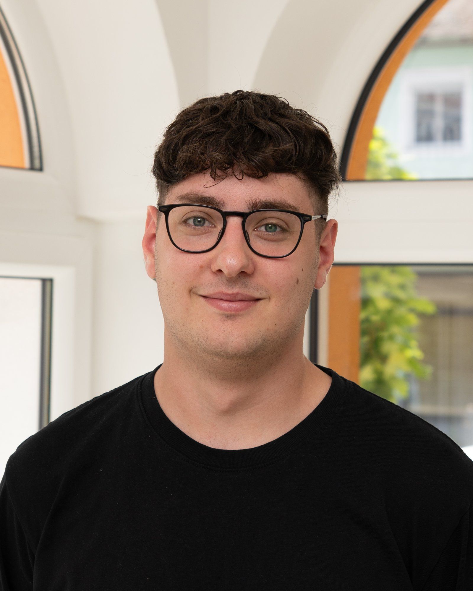 Porträt eines jungen Mannes mit dunklem Lockenhaar, Brille und schwarzem T-Shirt