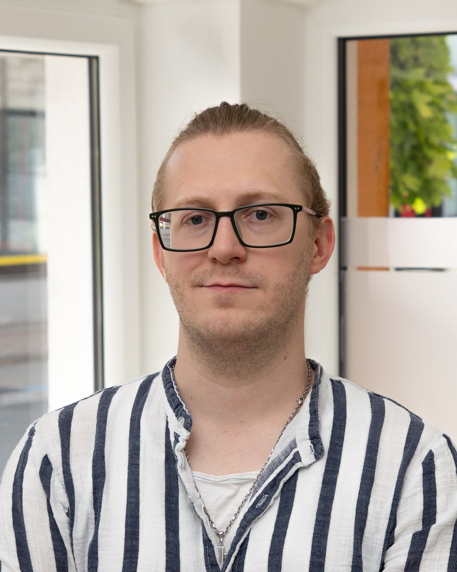 Porträt eines Mannes mit zurückgebundenem blondem Haar, Brille und gestreiftem Hemd